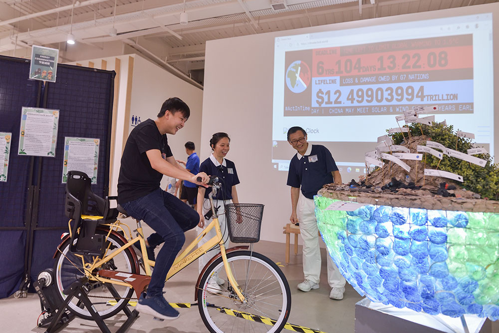 This year's environmental protection exhibition features interactive activities such as "Ride a bike to light up the Earth," effectively demonstrating the significance of environmental preservation. Simultaneously, a climate clock is projected on the wall serving as a constant reminder for individuals to make conscious efforts to reduce their carbon footprint. (Photo by Lai Tong Heng)